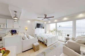A modern bedroom with a balcony, a bed with floral bedding, a white sofa, and a kitchen area with a microwave. - Perfect location and Unbelievable Views at Lahaina Roads (Lahaina)