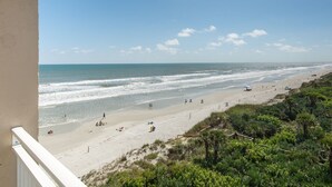 A beach view from a balcony with a clear sky, sandy beach, and sparse vegetation.
