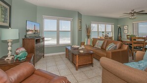 A living room with a television, a sofa, a coffee table, and a view of the beach.