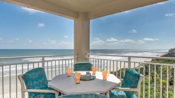 A balcony with a table and chairs overlooking a beach.