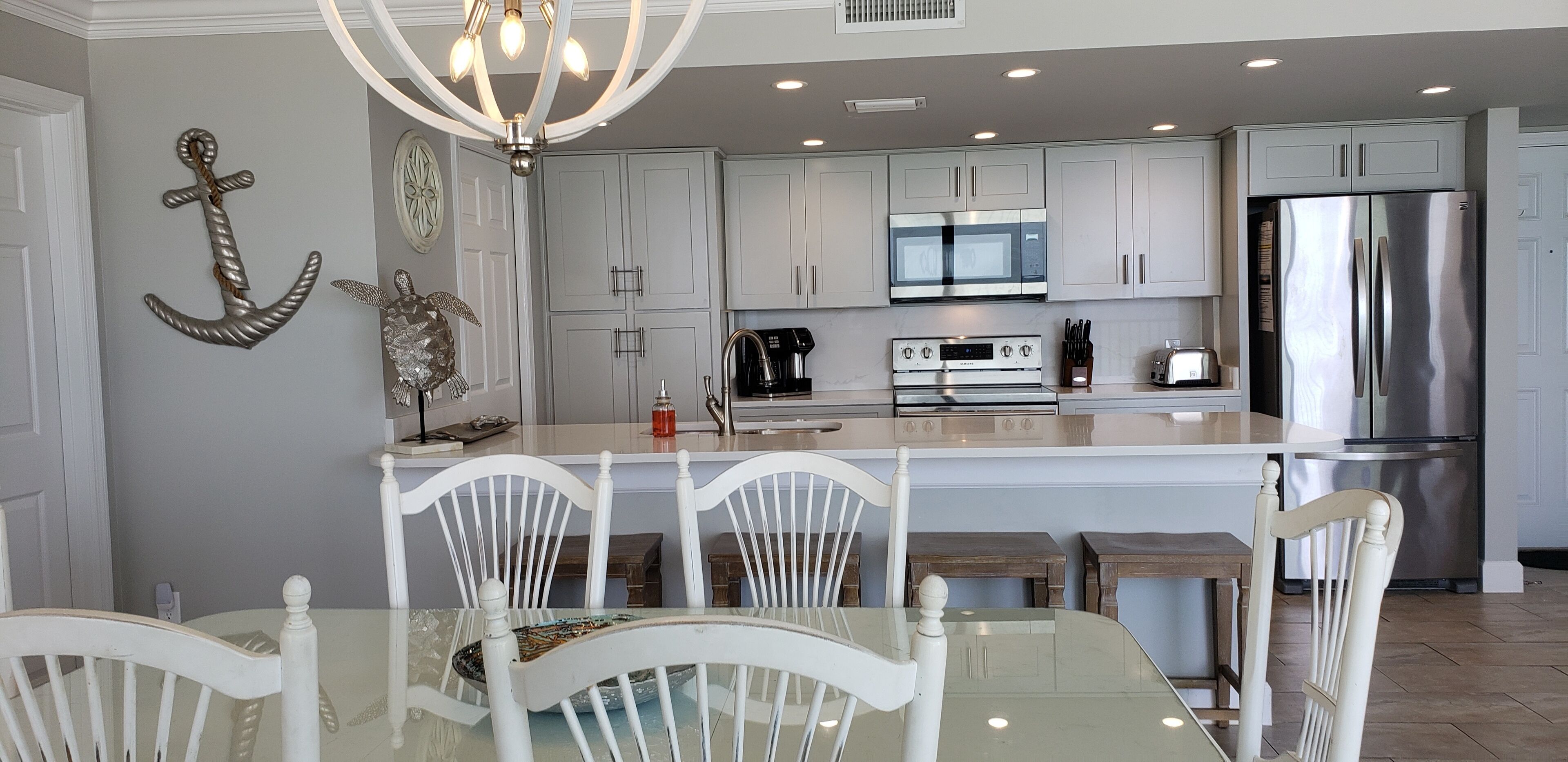 A modern kitchen with white cabinets, stainless steel appliances, and a glass dining table with white chairs.