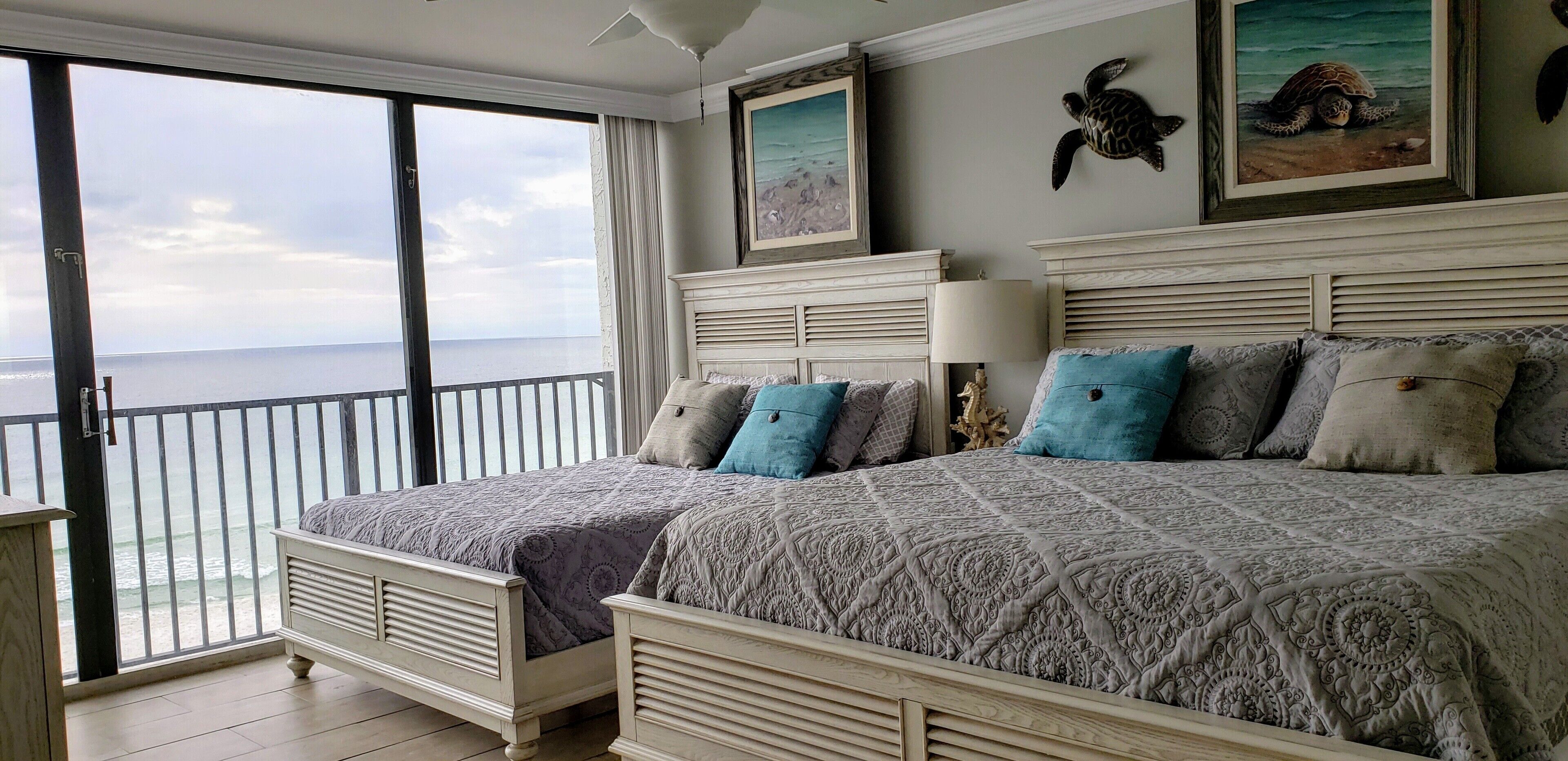 Un dormitorio con dos camas, un balcón con vista al mar y un cuadro de una tortuga en la pared.