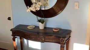 A wooden console table with a large mirror, a vase with white flowers, and a small decorative bowl. - Family and pet friendly close to beaches. SC Rental Permit 241396 (Santa Cruz)