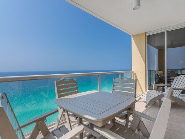 A balcony with a table and chairs, overlooking a clear blue sea. - Beautiful Condo with Amazing Views, Beach Service (Navarre)
