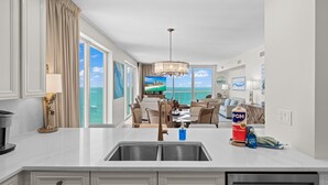 A modern kitchen with a large island, a dining area with a view of the ocean, and a chandelier. - Beautiful Condo with Amazing Views, Beach Service (Navarre)