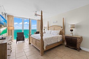 A four-poster bed with a view of the ocean, a desk with a lamp, and a bedside table with a lamp. - Beautiful Condo with Amazing Views, Beach Service (Navarre)