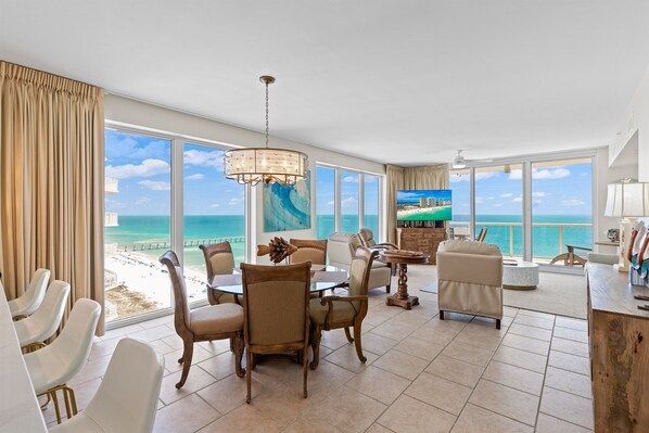 A spacious room with a large window overlooking the beach, a dining area with chairs and a table, and a view of the ocean. - Beautiful Condo with Amazing Views, Beach Service (Navarre)