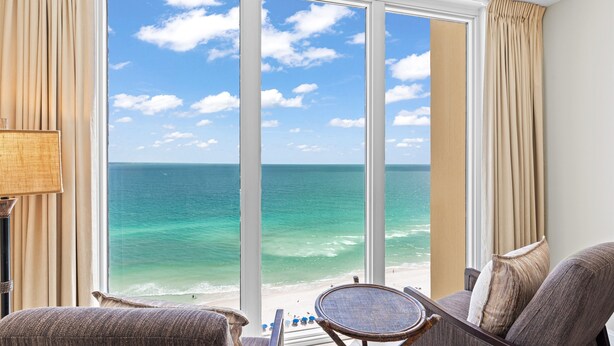A room with a large window offering a view of the ocean. There is a chair and a small table in the foreground. - Beautiful Condo with Amazing Views, Beach Service (Navarre)