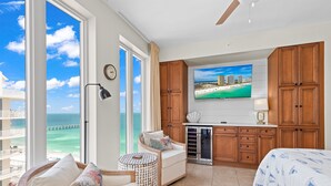 A hotel room with a large window overlooking the ocean, a bed, a seating area with a view, and wooden cabinets. - Beautiful Condo with Amazing Views, Beach Service (Navarre)