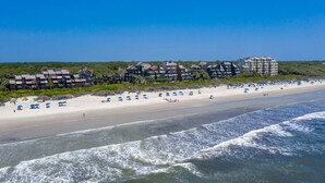 A beach with a row of beachfront condos, a sandy shore, and waves approaching the beach. - Windswept 4463! Oceanfront 3 BR Condo, Great Location! (Kiawah Island)