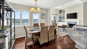 A dining area with a view of the ocean, a fireplace, and a television mounted on the wall. - Windswept 4463! Oceanfront 3 BR Condo, Great Location! (Kiawah Island)