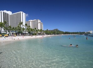 A beach with clear turquoise water, palm trees, and a large hotel building in the background. - 2 Bed 2 Bath Condo - Stunning Ocean views, Spacious, Clean and Comfortable (Honolulu)