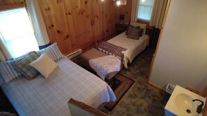 Una habitación con dos camas, un pequeño banco, una mesita de noche y un lavabo.