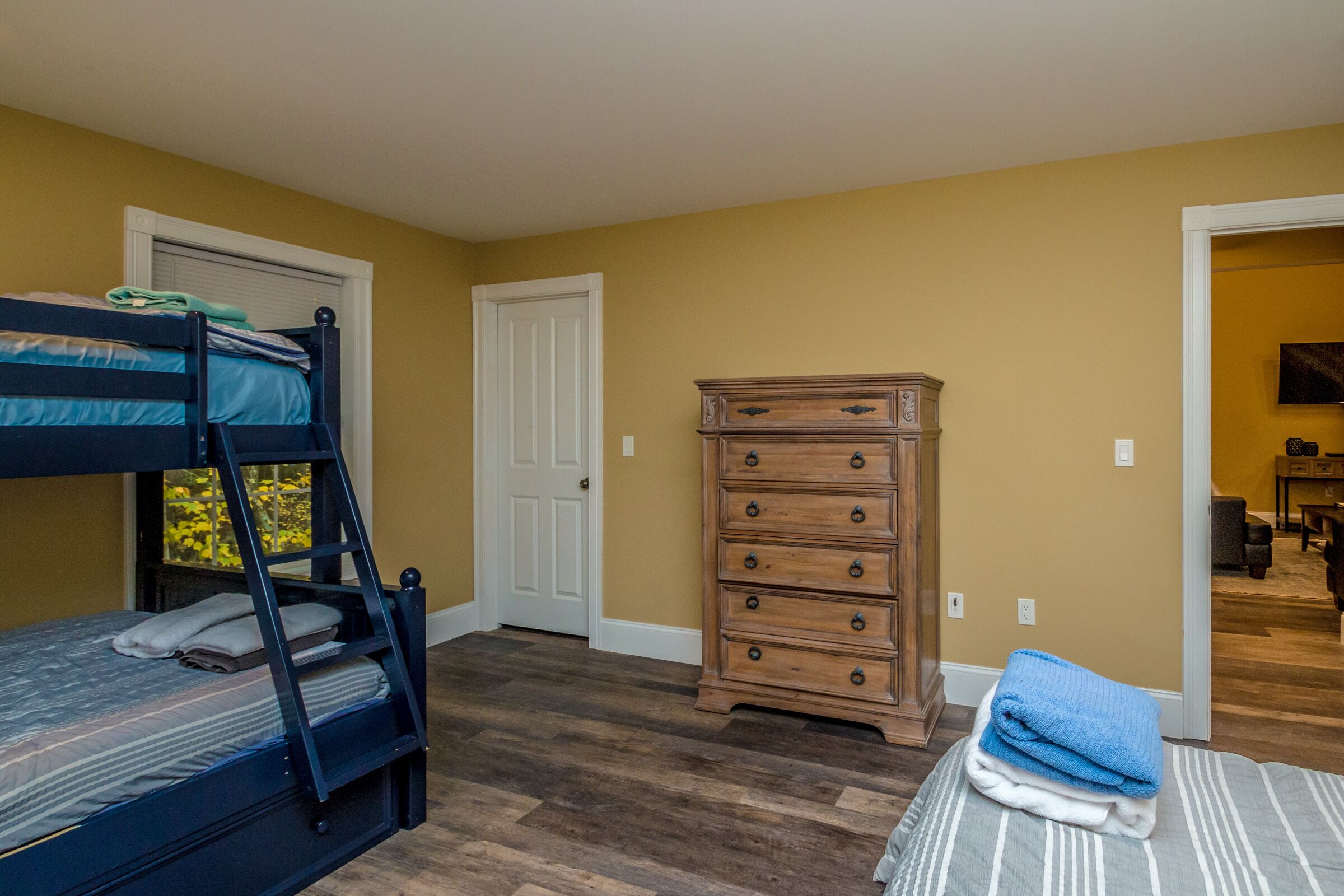 A bedroom with a bunk bed, a dresser, and a door leading to another room.