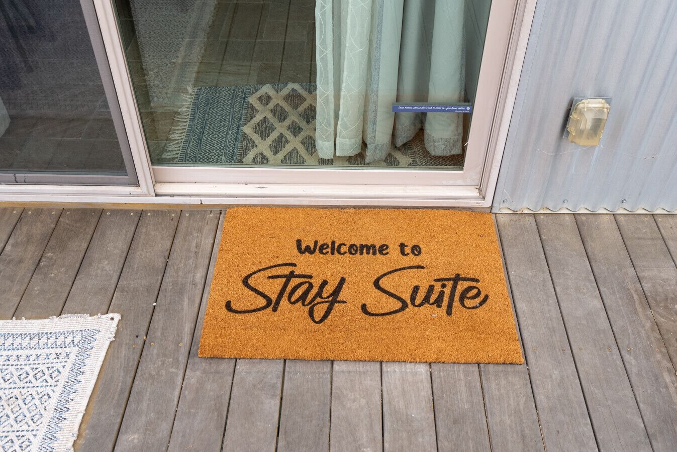A welcome mat with 'Welcome to Stay Suite' text in front of a sliding glass door.