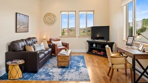 Una sala de estar con sofá, sillón, mesa de centro, mueble para televisión y un escritorio con silla.