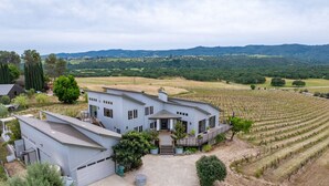 Un edificio amplio con garaje, patio cubierto y viñedo al fondo.