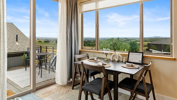 Un comedor con una mesa dispuesta para cuatro personas, vistas al campo y un gran ventanal corredizo que da a un patio exterior.