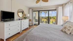 Un dormitorio con cama, televisión, ventilador de techo, cómoda y vistas al exterior.