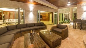 A modern lounge area with a curved sofa, wicker coffee tables, and a glass partition. - Bachelor Mansion Punta Cana - 24 GUEST - Luxury 9BR Villa Coral GATED Community (Bavaro)
