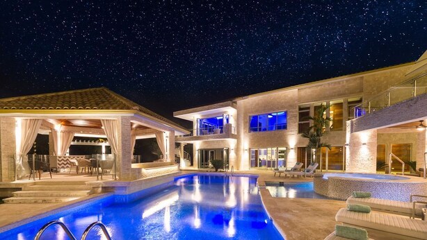 A modern pool area with a clear blue pool, a covered seating area, and a multi-level building with balconies. - Bachelor Mansion Punta Cana - 24 GUEST - Luxury 9BR Villa Coral GATED Community (Bavaro)