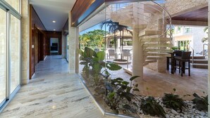 A modern hotel corridor with a glass wall, a spiral staircase, and outdoor seating. - Bachelor Mansion Punta Cana - 24 GUEST - Luxury 9BR Villa Coral GATED Community (Bavaro)