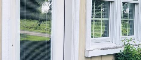 Una casa de fachada blanca, una ventana con persianas y un pequeño jardín con follaje.