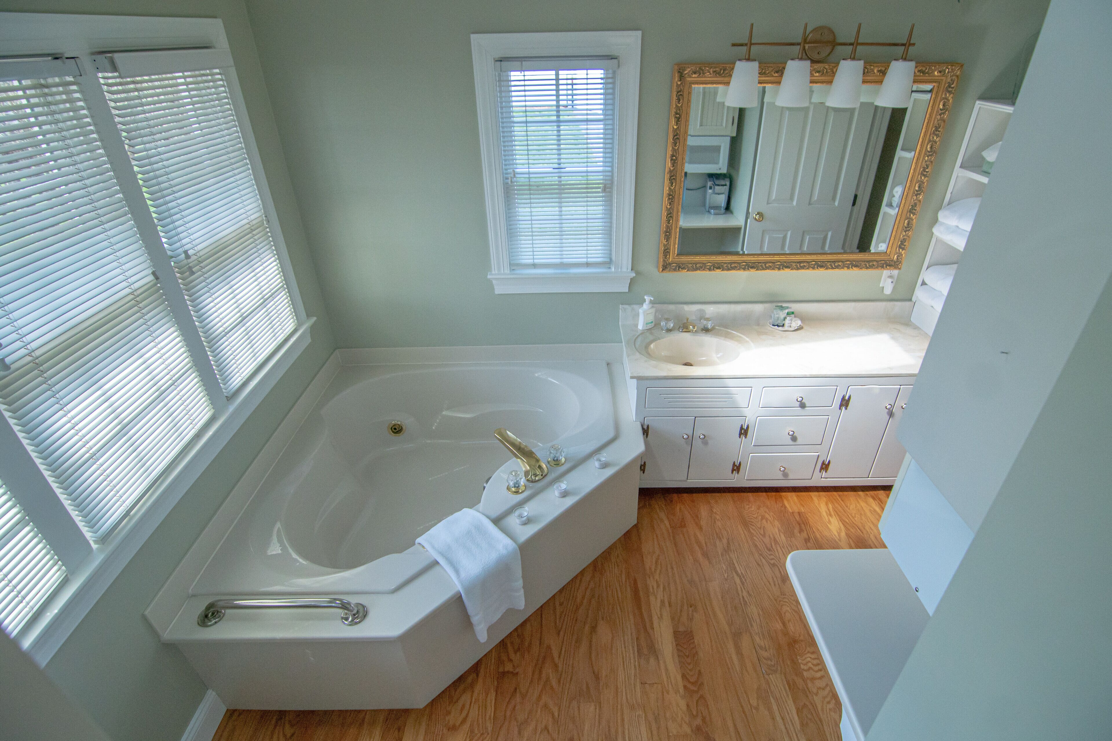 A bathroom with a large bathtub, a vanity with a mirror, and wooden flooring.