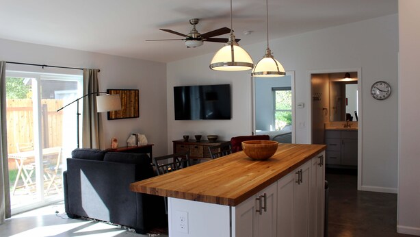 A modern kitchen with a wooden island, ceiling fan, pendant lights, and a dining area with a TV.
