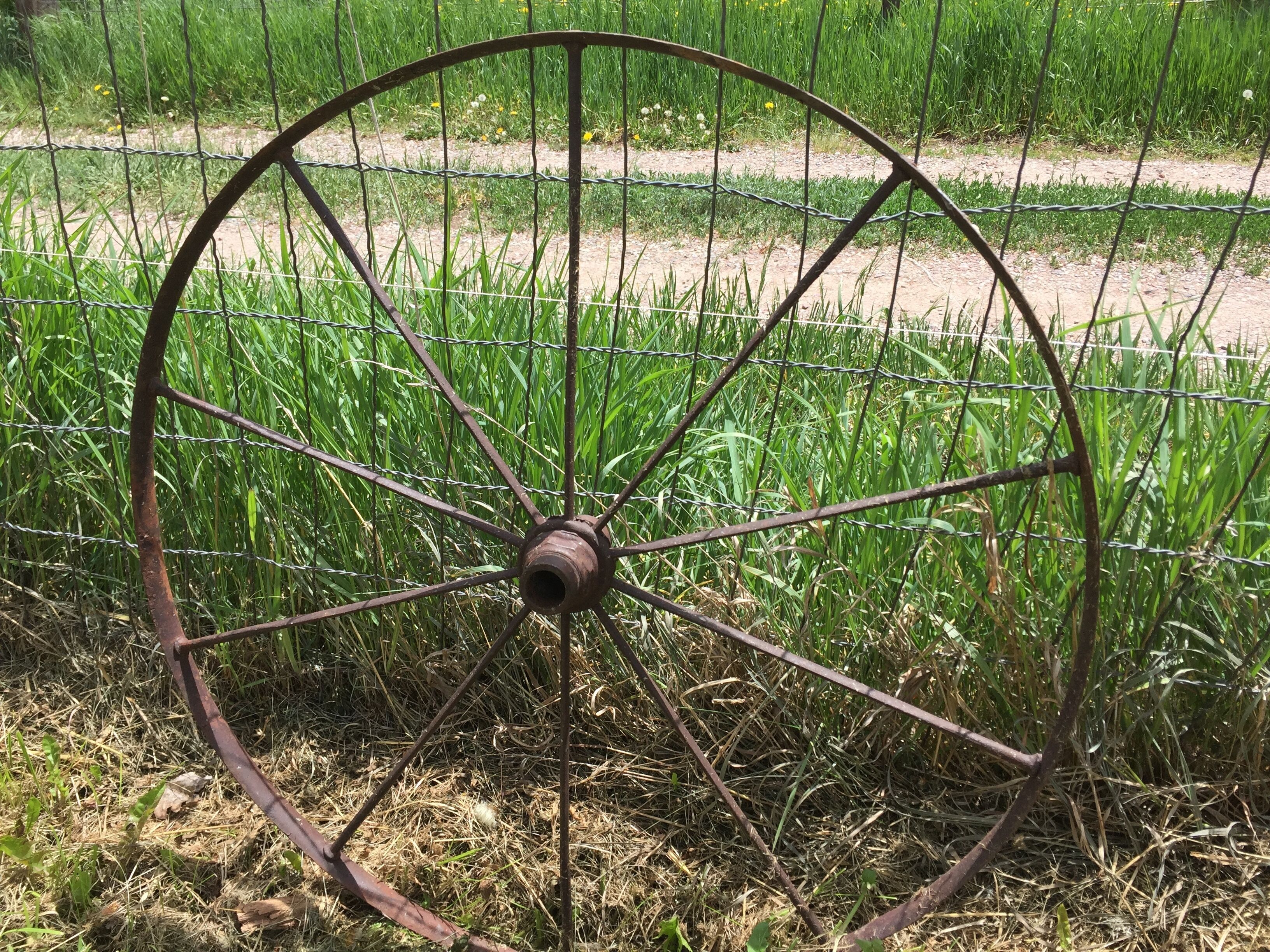 Una verja de metal oxidada en un campo con hierba alta y un camino de tierra.
