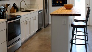 A modern kitchen with white cabinets, stainless steel appliances, a wooden island with a bowl, and a pendant light.