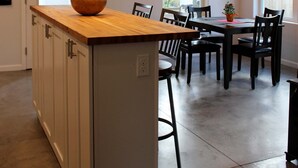 A modern kitchen with a wooden island, pendant lighting, and a dining area with chairs and a table.