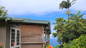 A coastal building with a balcony overlooking the sea, surrounded by lush greenery and vibrant flowers.
