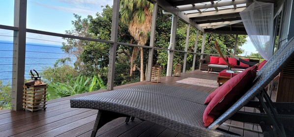 Un balcon avec une chaise en osier, un coussin rouge et une vue sur la mer.