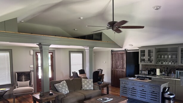 Un vaste espace de vie doté d’un haut plafond et d’un ventilateur de plafond, une cuisine avec un coin bar et un coin repas comprenant une table et des chaises.