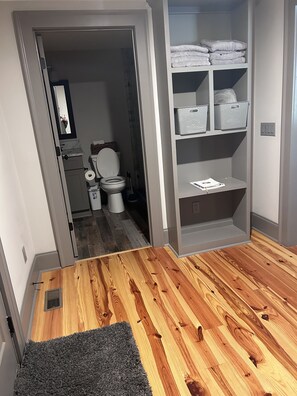 Bathroom features a toilet, toilet paper, and a storage area with towels and baskets.