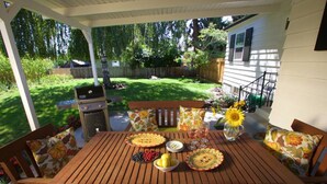 A wooden patio table with floral cushions, a grill, and a garden view. - Syvila’s Cottage | Private Garden Near Downtown (Walla Walla)