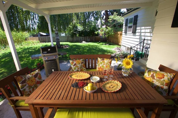 Ein Holztisch mit blumigen Kissen, ein Grill und Blick ins Grüne.