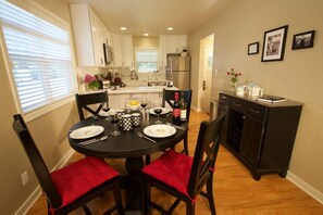A dining area with a round table, black chairs with red cushions, and a kitchen in the background.