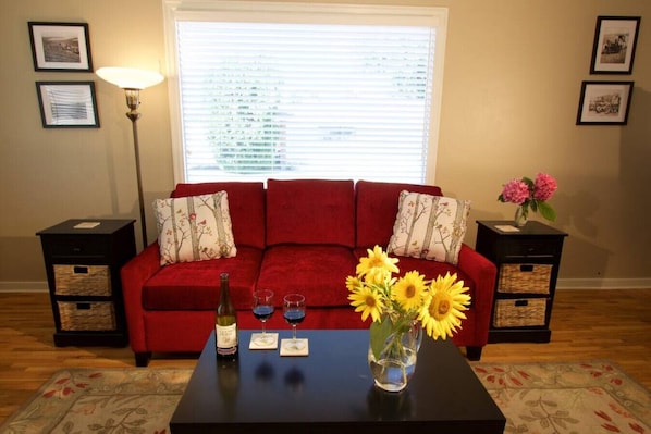 Un sofá rojo con cojines estampados, una mesa de centro con un jarrón de girasoles, una botella de vino y dos copas.