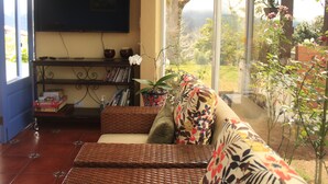 Ein Wohnzimmer mit einer Couch, einem an der Wand montierten Fernseher und einem Bücherregal mit Büchern und Dekorationsgegenständen.