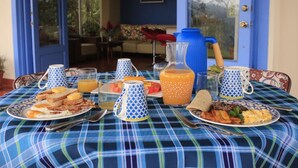 Ein Frühstückstisch mit verschiedenen Speisen, darunter Toast, Eier und Obst, auf einer blau-weißen karierten Tischdecke.