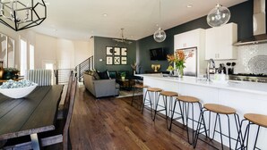 A modern kitchen with a central island, bar stools, and a dining area with a wooden table and benches. - Luxury Home in 12South, Downtown, Gulch, Music Row, Vandy / Roof Tops (Nashville)