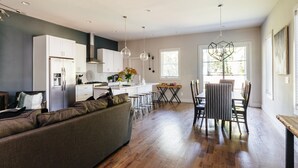 A modern kitchen with white cabinets, a dining area with a wooden table and chairs, and a sofa in the living area. - Luxury Home in 12South, Downtown, Gulch, Music Row, Vandy / Roof Tops (Nashville)