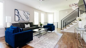 A modern living room with a sofa, armchairs, a coffee table, and a TV. - Luxury Home in 12South, Downtown, Gulch, Music Row, Vandy / Roof Tops (Nashville)
