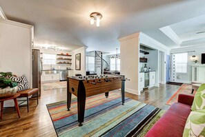 Amplia sala de estar con una mesa de fútbol de mesa, un sofá y una escalera que lleva a una cocina.