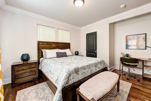 A bedroom with a wooden bed, bedside tables, a desk, and a chair.