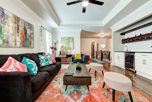 A spacious living room with a dark sofa, colorful cushions, a wooden coffee table, and a vibrant rug.