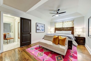 A bedroom with a bed, a sofa, a ceiling fan, and a patterned rug.