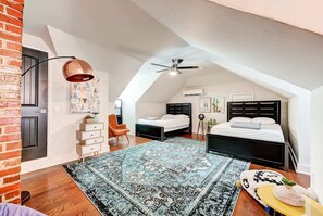Un dormitorio estilo loft con techo inclinado, una alfombra grande con estampado, una cama, un escritorio y una silla.